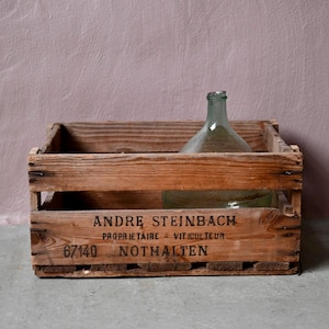 Puede incluir: Una caja de madera con el texto "ANDRE STEINBACH PROPRIETAIRE - VITICULTEUR 6740 NOTHALTEN" impreso en la parte delantera. Dos botellas de vidrio están dentro de la caja.