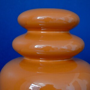 May include: A ceramic vase with a rounded, bulbous shape. The vase is a deep orange color and has a glossy finish.
