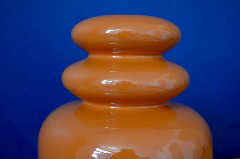 May include: A ceramic vase with a rounded, bulbous shape. The vase is a deep orange color and has a glossy finish.