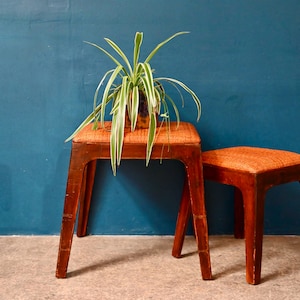 Peut inclure: Deux tabourets en bois avec des sièges en osier brun. Les tabourets sont devant un mur bleu et une plante en pot avec des feuilles vertes et blanches.