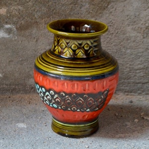 Może przedstawiać: Brązowy i pomarańczowy ceramiczny wazon z geometrycznym wzorem. Wazon ma szeroką podstawę i wąską szyjkę.