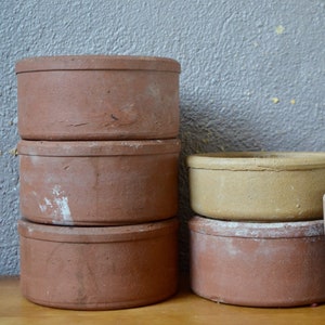 Könnte beinhalten: Ein Stapel aus vier Terrakotta-Töpfen, zwei sind braun und zwei sind in einer helleren braunen Farbe. Die Töpfe sind auf einer Holzoberfläche gestapelt. Ein kleiner Terrakotta-Topf mit einer grünen Sukkulente ist im Hintergrund.