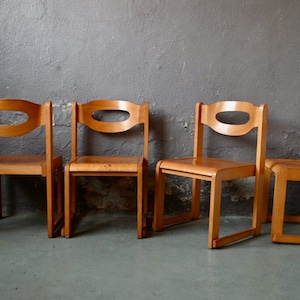 May include: Four wooden chairs with a simple design. Each chair has a curved back with a cutout and four legs.