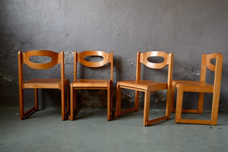 May include: Four wooden chairs with a simple design. Each chair has a curved back with a cutout and four legs.