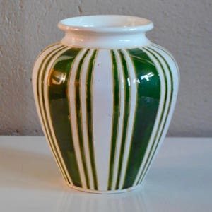 May include: A white ceramic vase with green and gold stripes. The vase has a rounded body and a narrow neck.