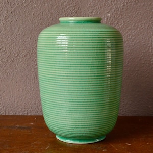 May include: A green ceramic vase with horizontal striped detailing. The vase has a rounded body and a slightly flared rim. The vase is approximately 25 cm tall.