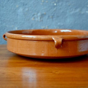 Puede incluir: Un plato de servir de terracota con dos asas. El plato es redondo y tiene un borde ligeramente elevado.