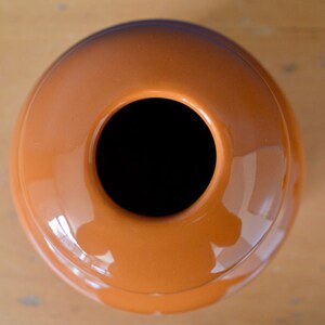 May include: A round, orange ceramic vase with a wide opening at the top. The vase has a smooth, glossy finish.