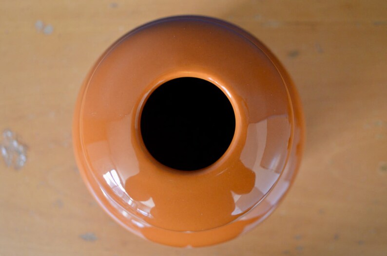 May include: A round, orange ceramic vase with a wide opening at the top. The vase has a smooth, glossy finish.