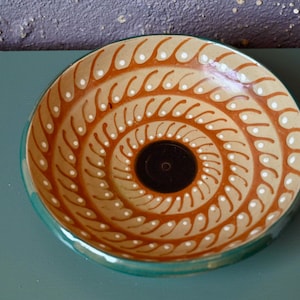 May include: A ceramic bowl with a green rim and a brown and white swirl pattern. The bowl has a black centre.
