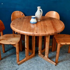 May include: A round wooden table with four chairs. The table and chairs are made of light brown wood. There is a blue and white ceramic jug and a blue and white ceramic cup on the table.