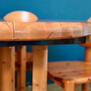 May include: A round wooden table with a natural wood finish and a black top. The table has four legs and is surrounded by two chairs with a similar wood finish.