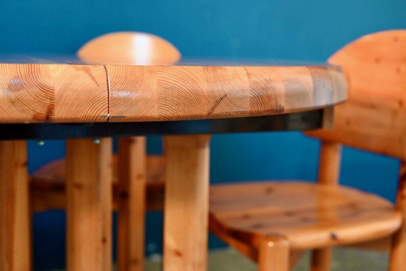 May include: A round wooden table with a natural wood finish and a black top. The table has four legs and is surrounded by two chairs with a similar wood finish.
