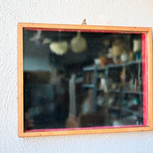 May include: A wooden framed mirror with a red border and a blurry reflection of a room with shelves.