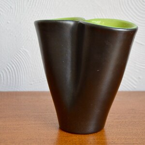 May include: A black ceramic vase with a green rim. The vase has a unique, abstract shape.
