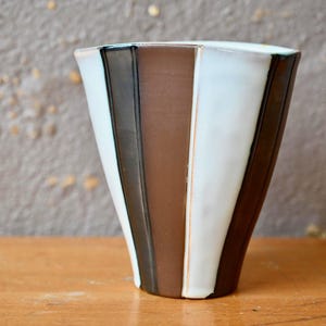 May include: A white ceramic vase with brown and black vertical stripes. The vase has a flared opening and a rounded bottom.