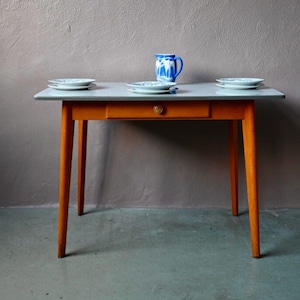 Peut inclure: Petite table à pieds orange et plateau gris, avec un tiroir, une tasse et des assiettes en céramique bleu et blanc. La table mesure environ 76 cm de long et 51 cm de large. Les assiettes et la tasse ont un motif bleu et blanc.