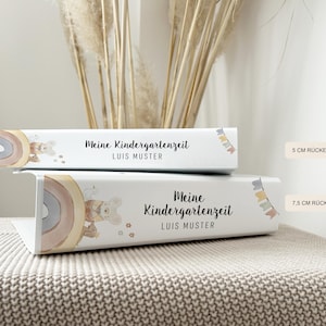 May include: Two white binders with colourful rainbow and animal illustrations. The text on the binders reads "Meine Kindergartenzeit" and "LUIS MUSTER". The binders are 5 cm and 7.5 cm wide.