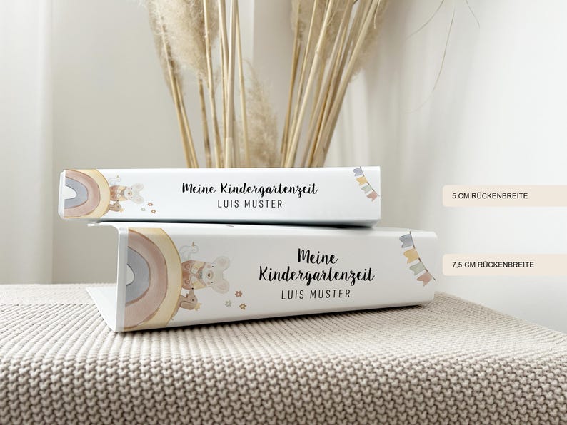 May include: Two white binders with colourful rainbow and animal illustrations. The text on the binders reads "Meine Kindergartenzeit" and "LUIS MUSTER". The binders are 5 cm and 7.5 cm wide.