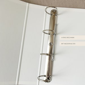 May include: White binder with a silver 4-ring mechanism and a metal clip. The binder has the text "4-RING MECHANIK" and "MIT NIEDERHALTER" printed on it.