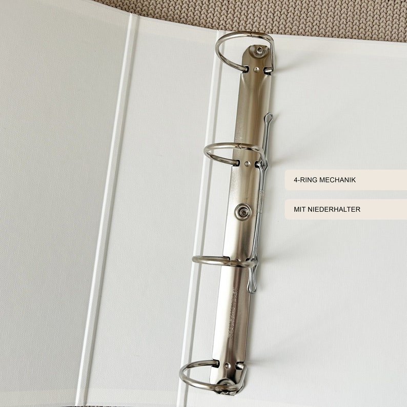 May include: White binder with a silver 4-ring mechanism and a metal clip. The binder has the text "4-RING MECHANIK" and "MIT NIEDERHALTER" printed on it.