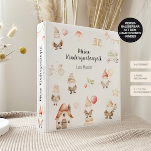 Könnte beinhalten: Ein weißer Ordner mit einem personalisierten Titel, der "Meine Kindergartenzeit" und "Luis Muster" lautet. Der Ordner hat ein verspieltes Design mit Gnomen, einem Haus, einem Fahrrad und anderen Illustrationen. Der Ordner ist im A4-Format und hat einen 2-Ring-Mechanismus mit einem 14,6 cm breiten Rücken.