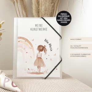 Könnte beinhalten: Ein transparenter Kunststoffordner mit schwarzem Gummizug. Der Einband zeigt eine Aquarellillustration eines Mädchens, einen Regenbogen und den Text "MEINE KUNSTWERKE". Der Ordner hat das Format A4/A3 und fasst ca. 150 Blatt.