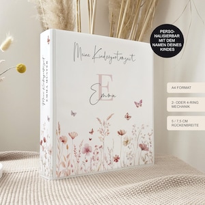 Könnte beinhalten: Ein weißer Ordner mit einem Blumenmuster und dem Text "Meine Kindergartenzeit" und "Emma" in Rosa. Der Ordner ist im A4-Format und hat einen 2- oder 4-Ring-Mechanismus. Der Rücken ist 5,75 Zoll breit.