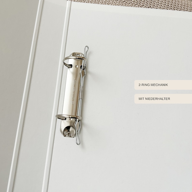 May include: A white binder with a silver 2-ring mechanism and a silver metal clip. The binder has the text "2-RING MECHANIK" and "MIT NIEDERHALTER" printed on it.