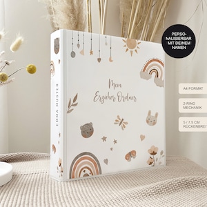 Könnte beinhalten: Ein weißer Ordner mit einem personalisierten "Mein Erzieher Ordner" Design. Der Einband zeigt einen Regenbogen, Sonne, Sterne, Schmetterlinge und Bären in Braun-, Beige- und Rosatönen. Der Ordner ist im A4-Format mit einem 2-Ring-Mechanismus und einem 5,75 Zoll breiten Rücken.