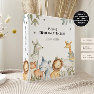 Könnte beinhalten: Ein weißer Ordner mit einer bunten Illustration von Tieren, darunter ein Zebra, eine Giraffe, ein Tiger, ein Nashorn und ein Löwe. Der Ordner trägt den Titel "Meine Kindergartenzeit" mit dem Namen "Juliane Muster" darunter. Der Ordner ist personalisierbar mit dem Namen Ihres Kindes. Er ist im A4-Format, hat eine 2-Ring-Mechanik und ist 14,6 cm breit.