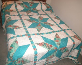 May include: A white and teal blue quilt with a star pattern. The quilt is made with a floral fabric and has a quilted texture.