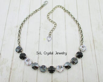 Puede incluir: Un collar de cadena plateada con un dije de corazón plateado y una fila de cuentas de cristal negro y transparente. El collar está sobre un fondo de madera blanca. "Söl Crystal Jewelry" está escrito en texto negro sobre el fondo.