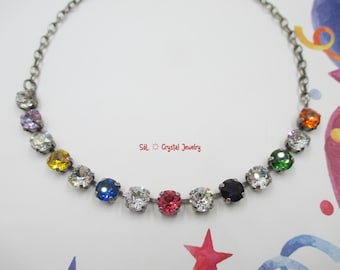 Puede incluir: Un collar de cadena de plata con un arcoíris de cristales de colores. Los cristales están engastados en plata y están rodeados de cristales transparentes. El collar está sobre un fondo blanco.