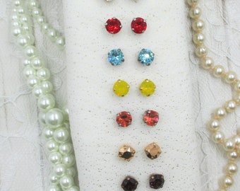 May include: A set of 10 pairs of colorful crystal earrings displayed on a white background. The earrings are arranged in rows, with each row featuring a different color. The colors include clear, white, red, blue, yellow, orange, gold, brown, and light blue.