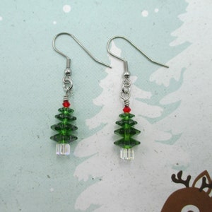 May include: A pair of silver earrings with green crystal Christmas tree charms. The trees have a red crystal at the top.