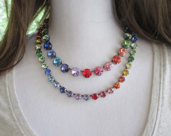 May include: A rainbow-coloured crystal necklace with a silver chain. The necklace is made up of round, faceted crystals in a variety of colours, including red, orange, yellow, green, blue, indigo, and violet.