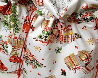May include: Two white drawstring gift bags with a festive Christmas print. The fabric features illustrations of wrapped presents, women in red dresses, and Christmas trees. The bags have red drawstrings and a silver dotted lining.