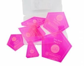 May include: A collection of bright pink acrylic quilting templates in various geometric shapes, including pentagons and triangles. Each template is labeled with text, including "Tula Nova Piece F" and "PaperPieces.com". The templates are in a clear plastic container.