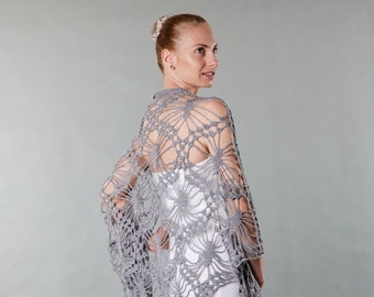 May include: A gray crocheted shawl with a delicate floral pattern. The shawl is draped over a person's shoulders and is made of a lightweight, airy yarn.