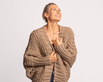 May include: A dark beige knitted cardigan with a relaxed fit and long sleeves. The cardigan is open in the front and has a textured knit pattern.
