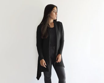 May include: A woman wearing a black long-sleeved cardigan with a draped hemline, black skinny jeans, and black ankle boots.