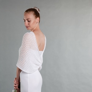 May include: White crochet bridal shawl with a delicate openwork pattern. The shawl is draped over the shoulders and back of a person wearing a white dress.