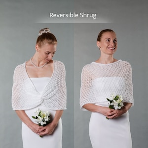 May include: White crocheted shrug with a delicate openwork pattern. The shrug is reversible, showing a different texture on each side. The model is wearing a white dress and holding a small bouquet of white flowers.