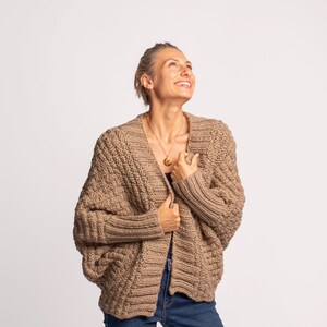 May include: A dark beige knitted cardigan with a relaxed fit and long sleeves. The cardigan is open at the front and has a textured knit pattern.