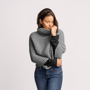 May include: A gray knitted turtleneck sweater with a loose fit and a textured pattern. The sweater is worn with blue jeans.