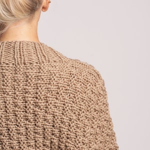 May include: A dark beige knitted jumper with a cable knit pattern.