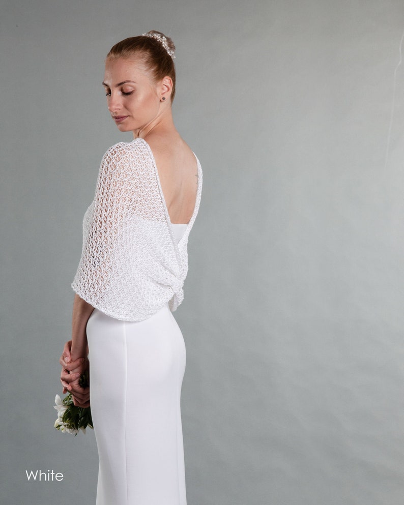 May include: White crochet bridal shawl with a delicate openwork pattern. The shawl is draped over the shoulders and back of a person wearing a white dress.