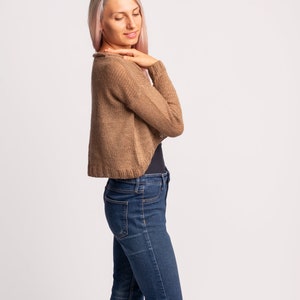 May include: A woman wearing a brown knitted cardigan with long sleeves and blue jeans.