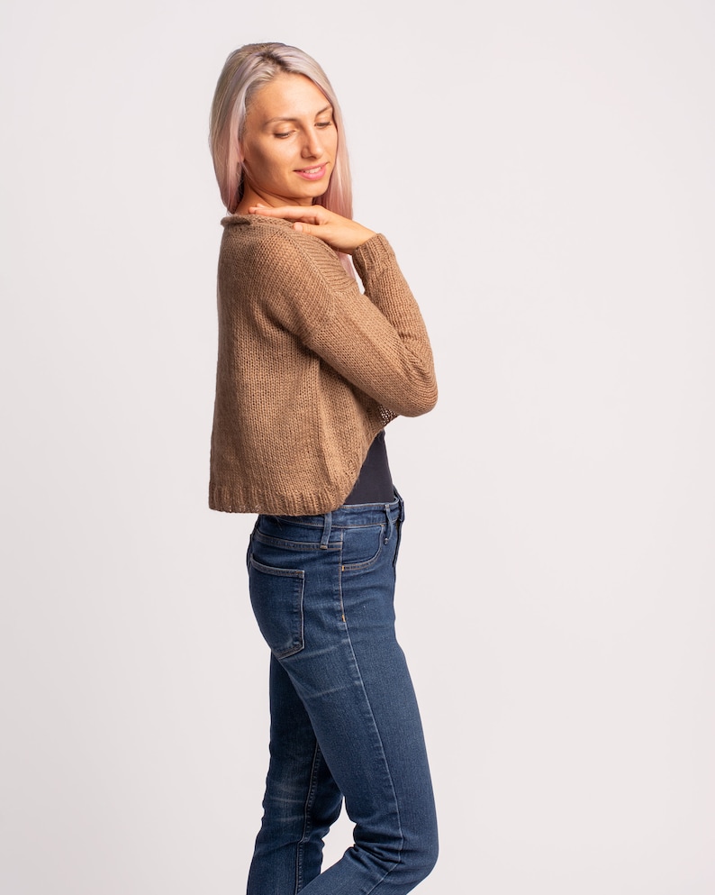 May include: A woman wearing a brown knitted cardigan with long sleeves and blue jeans.